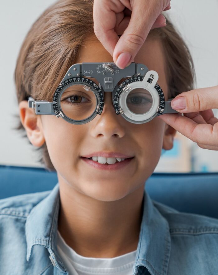 Young boy with phoropter during sight testing eye examinations in ophthalmological clinic.